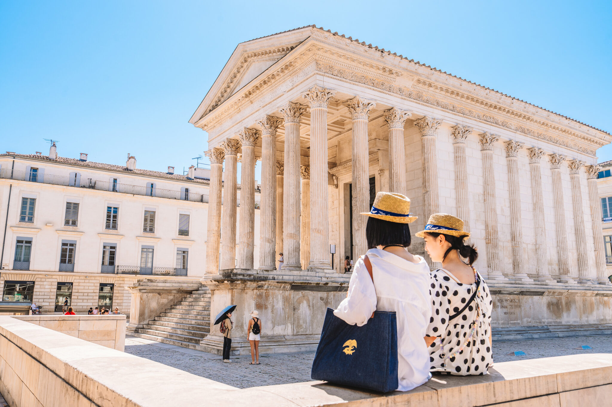 Deux visiteuses face à la Maison Carrée de Nîmes sous un ciel bleu, ambiance printanière.
